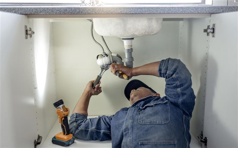 Plumber repairing pipes beneath a bathroom sink in San Francisco